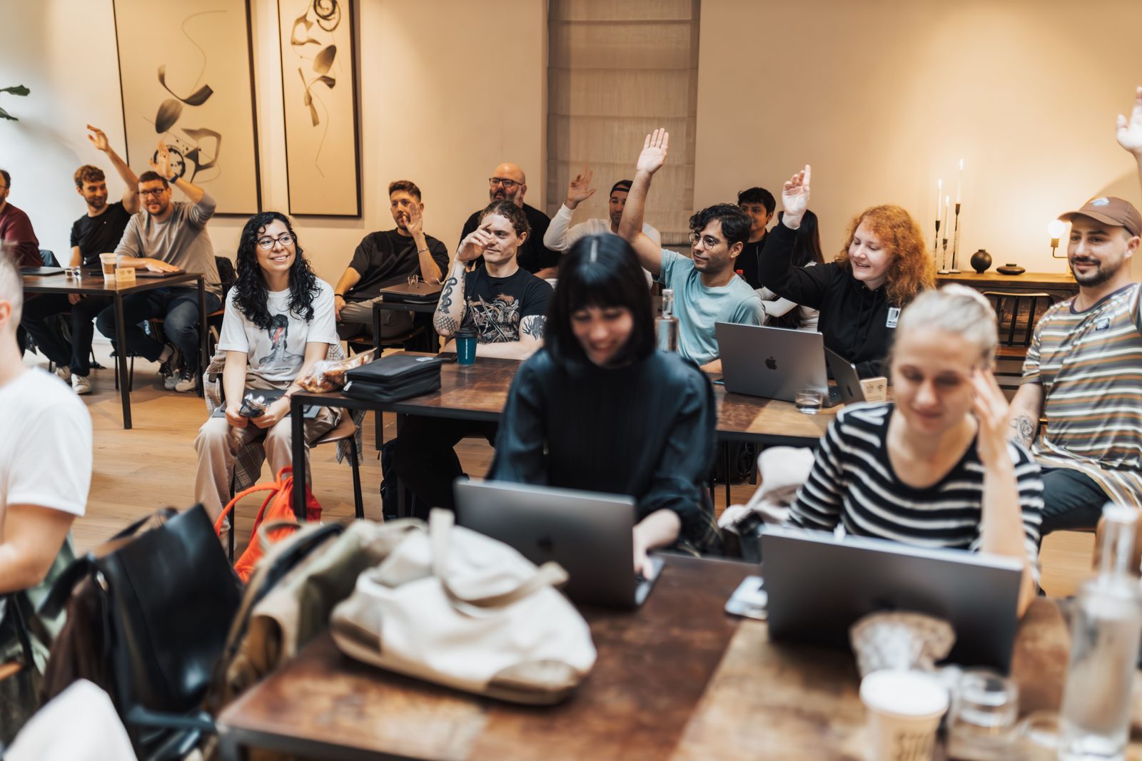 Seminargruppe an Tischen mit Laptops, mehrere Teilnehmende melden sich per Handzeichen